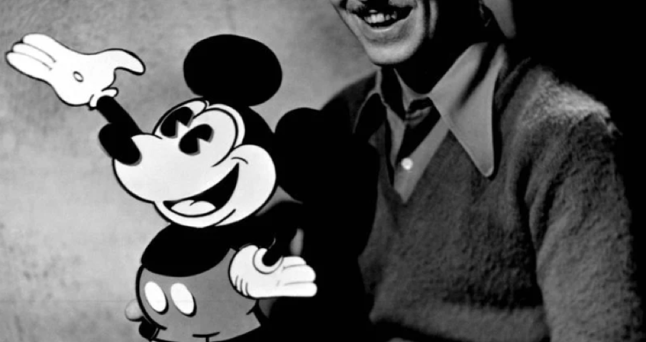 Une personne est assise à côté d'une découpe de Mickey Mouse, souriant à la caméra, célébrant avec joie la naissance du personnage bien-aimé le 18 novembre 1928.