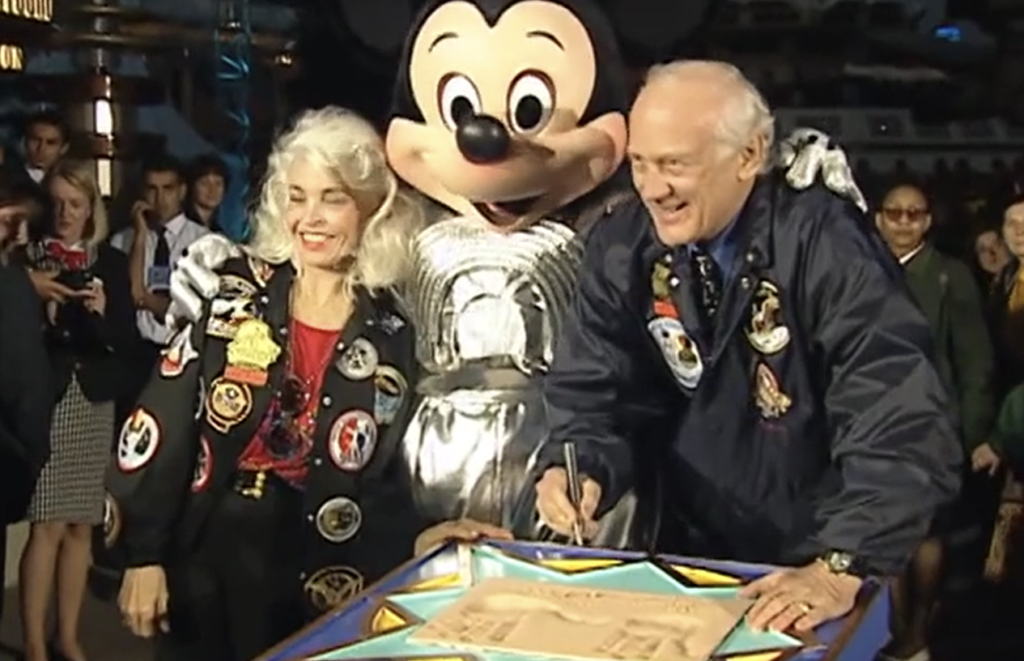 Une femme et un homme signent un document tandis que quelqu'un en costume de Mickey Mouse se tient derrière eux, tout souriant, rappelant la joie du 31 mai 1995 lorsque Space Mountain a ouvert ses portes aux amateurs de sensations fortes.