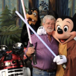 Un homme brandit deux sabres laser, posant avec Mickey Mouse en tenue de Jedi, Minnie déguisée en princesse Leia et un R2-D2 portant des oreilles de Mickey. Dingo est en arrière-plan, capturant l'essence ludique de Star Wars juste après son rachat le 30 octobre 2012.