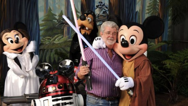 Un homme brandit deux sabres laser, posant avec Mickey Mouse en tenue de Jedi, Minnie déguisée en princesse Leia et un R2-D2 portant des oreilles de Mickey. Dingo est en arrière-plan, capturant l'essence ludique de Star Wars juste après son rachat le 30 octobre 2012.