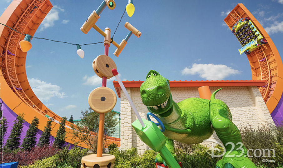 Une grande figurine de dinosaure vert de Toy Story se tient à côté de jouets surdimensionnés dans un parc à thème extérieur, avec des montagnes russes orange vif serpentant à l'arrière-plan.