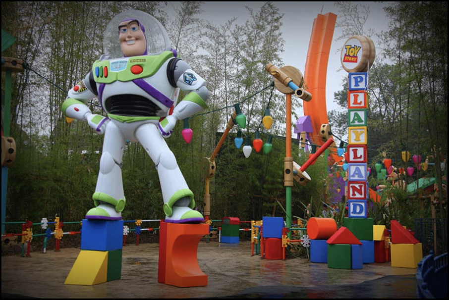 Une grande statue de Buzz l'Éclair se dresse à l'entrée de Toy Story Playland, entourée de blocs colorés, de décorations Toy Story et d'un panneau avec des lettres empilées.