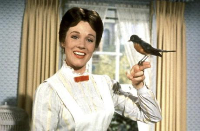 Une femme en robe blanche sourit en tenant un oiseau perché sur son doigt, lui offrant peut-être un morceau de sucre, devant une fenêtre aux rideaux beiges.