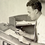 Un homme en chemise est assis à une table à dessin, dessinant ou écrivant sur du papier avec un stylo, rappelant Ub Iwerks au travail sur ses animations emblématiques.