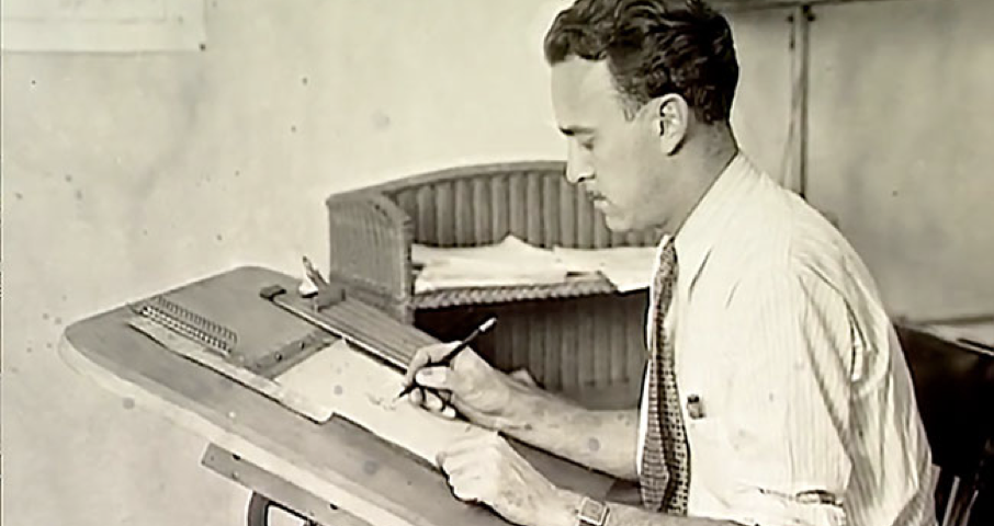Un homme en chemise est assis à une table à dessin, dessinant ou écrivant sur du papier avec un stylo, rappelant Ub Iwerks au travail sur ses animations emblématiques.