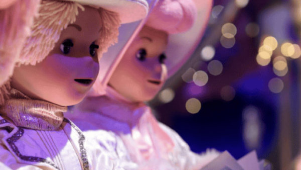 Gros plan de deux poupées vêtues de costumes et de chapeaux blancs, tenant des livres, avec de douces lumières violettes et jaunes en arrière-plan, évoquant une scène fantaisiste inspirée du style signature de Mary Blair.