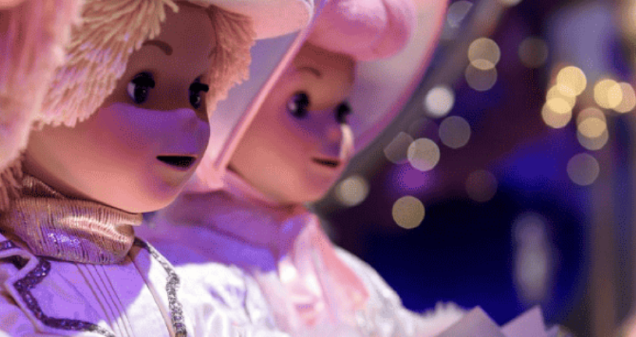 Gros plan de deux poupées vêtues de costumes et de chapeaux blancs, tenant des livres, avec de douces lumières violettes et jaunes en arrière-plan, évoquant une scène fantaisiste inspirée du style signature de Mary Blair.