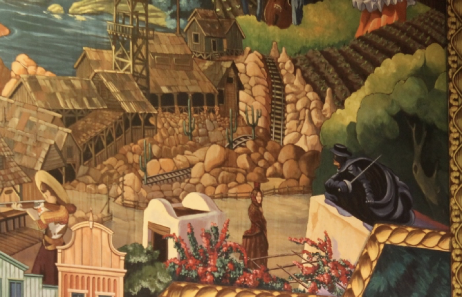 Un tableau représente un village rustique avec des bâtiments en bois, un terrain rocheux, un vignoble et plusieurs personnages, dont Zorro dans un manteau sombre observant silencieusement depuis un toit.