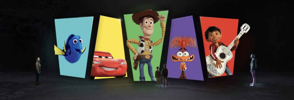 Cinq personnes se tiennent face à de grands écrans affichant les personnages bien-aimés de Pixar : Dory, Flash McQueen, Woody, une créature ressemblant à Muppet et un garçon avec une guitare.