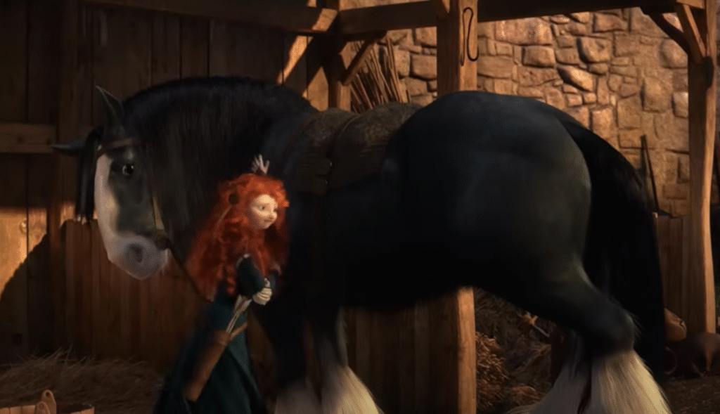 Une fille rebelle aux longs cheveux roux bouclés marche à côté d'un grand cheval noir aux marques blanches dans une écurie en bois aux murs en pierre.