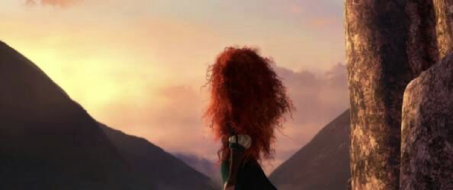 Un rebelle aux longs cheveux roux bouclés se tient sur un rebord rocheux, regardant vers le ciel au-dessus des montagnes au coucher du soleil.