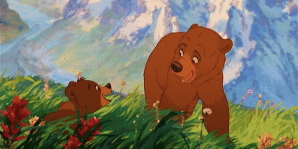 Deux ours bruns animés interagissent dans un champ d'herbe avec des fleurs colorées, avec pour toile de fond des sommets montagneux et un ciel bleu, rappelant Mon Frère Ours de la galaxie Disney.