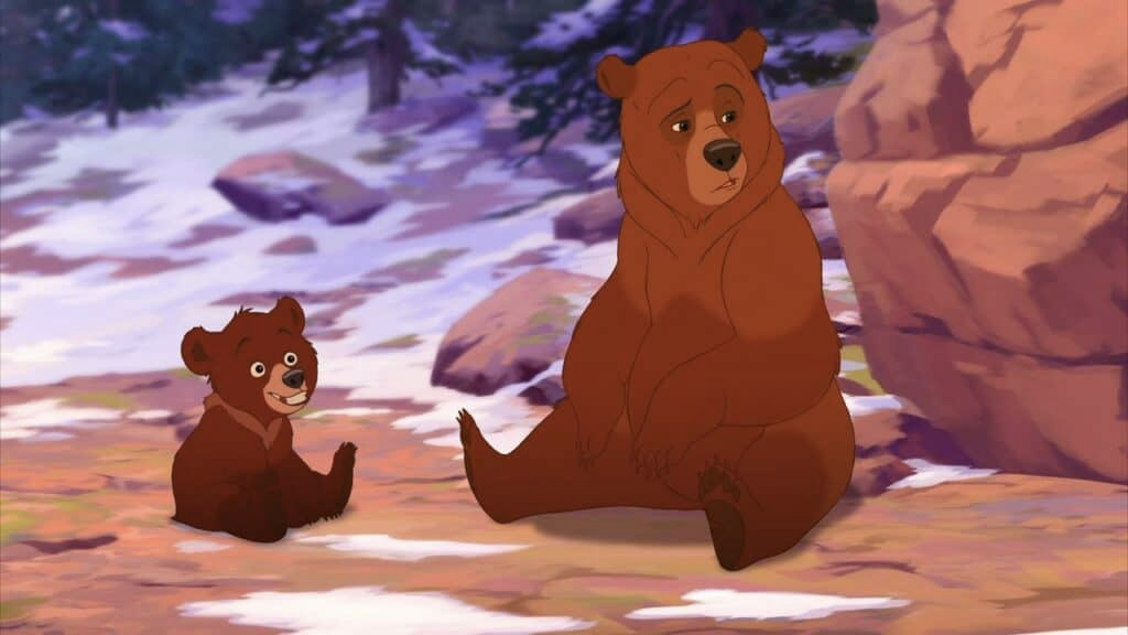 Deux ours animés, un adulte et un ourson de Mon Frère Ours, sont assis sur le sol enneigé d'une forêt, avec des arbres et des rochers en arrière-plan, évoquant la magie d'une galaxie Disney.