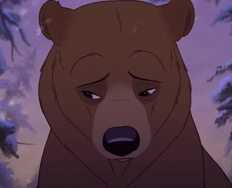Un ours animé à la fourrure brune regarde vers le bas avec une expression triste sur un fond neigeux aux tons violets, évoquant l'esprit chaleureux de Mon Frère Ours de la galaxie Disney.