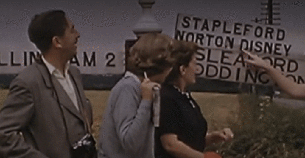 Trois personnes se tiennent à l'extérieur, regardant un panneau routier indiquant les directions de Stapleford, Norton Disney, Sleaford et Oddington, tandis qu'une autre personne pointe vers le panneau - évoquant l'esprit d'une chasse au trésor sur l'Île au Trésor.