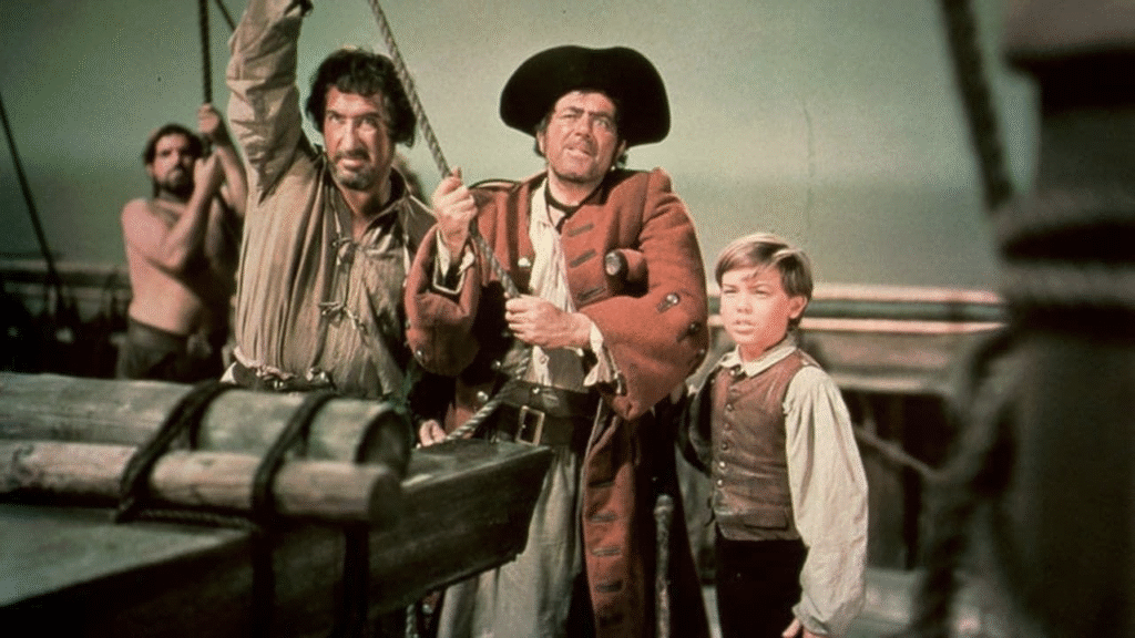 Trois personnes en tenue de pirate d'époque se tiennent sur le pont d'un bateau en bois, entourées de cordes et d'équipements, sous un ciel nuageux, rappelant l'esprit d'aventure de l'Île au Trésor.