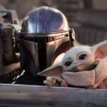 Une personne en armure mandalorienne est assise à côté de Grogu, le petit extraterrestre vert aux grandes oreilles, tous deux à l'intérieur d'un vaisseau spatial de l'univers cinématographique de Star Wars.