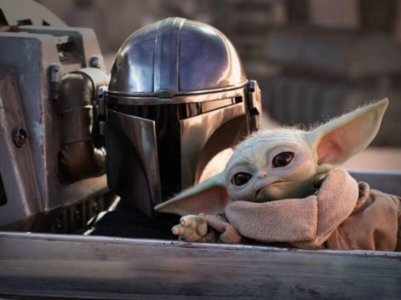 Une personne en armure mandalorienne est assise à côté de Grogu, le petit extraterrestre vert aux grandes oreilles, tous deux à l'intérieur d'un vaisseau spatial de l'univers cinématographique de Star Wars.