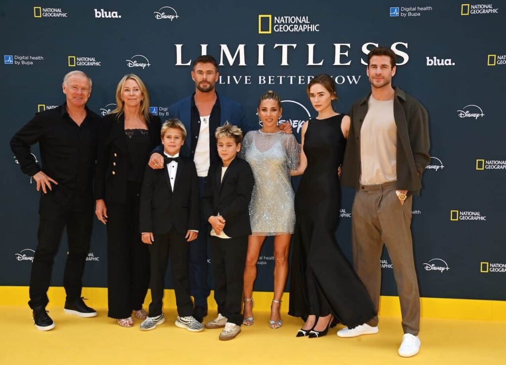 Sept adultes et deux enfants posent pour une photo de groupe sur un tapis jaune devant une toile de fond de l'événement National Geographic "Limitless", célébrant la série Disney+ avec Chris Hemsworth.