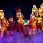 Cinq personnages de Disney en costumes d'Halloween se tiennent dans une rue décorée la nuit pendant Disneyland Halloween 2025, avec du brouillard au sol et des lumières festives en arrière-plan.