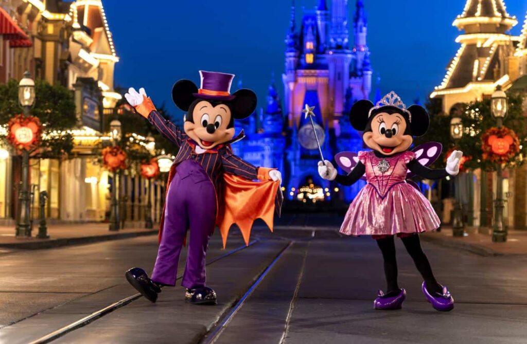 Mickey Mouse et Minnie Mouse, vêtus de costumes d'Halloween, posent dans une rue décorée d'un parc d'attractions, avec un château en arrière-plan, lors de la fête d'Halloween "Mickey's Not So Scary".