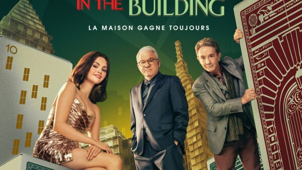 Trois personnes en tenue de soirée posent parmi des cartes à jouer et des dés surdimensionnés, avec de grands immeubles en arrière-plan et le texte "IN THE BUILDING" au-dessus d'eux - une scène de Only Murders In The Building Saison 5, disponible sur Disney+.