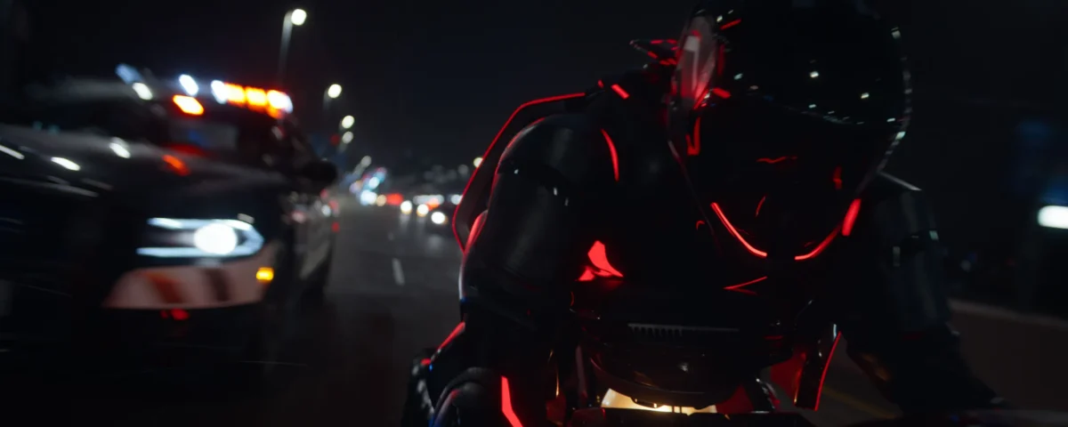 Une personne vêtue d'une combinaison noire futuriste avec des lumières rouges conduit une moto la nuit, poursuivie par une voiture de police dans une rue de la ville - évoquant les scènes de poursuite high-tech vues dans Tron : Ares de Disney avant sa date de sortie.