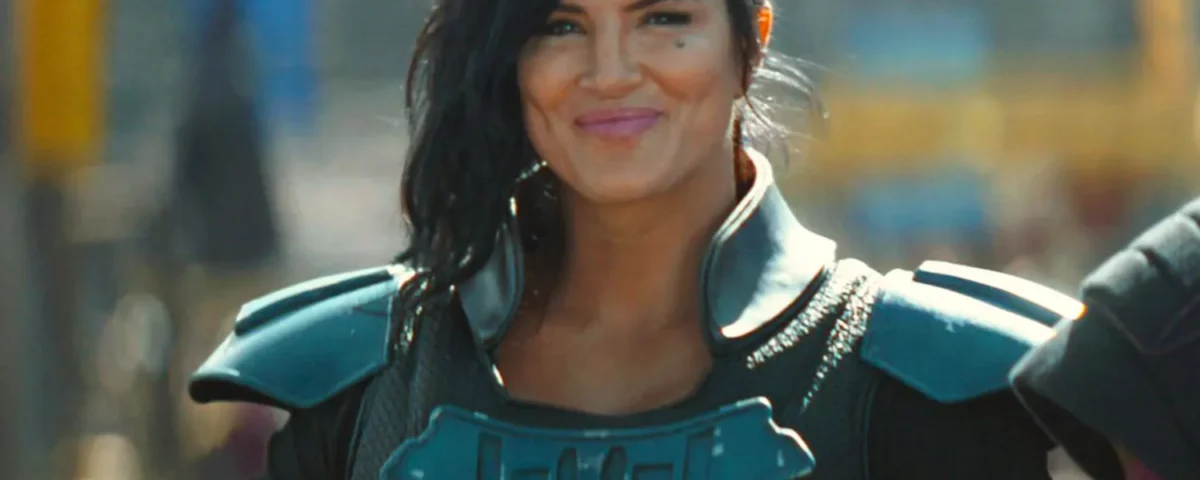 Personne vêtue d'une armure futuriste avec des épaulettes, cheveux noirs coiffés sur le côté, debout à l'extérieur et souriante, rappelant le personnage emblématique de Gina Carano chez Disney.