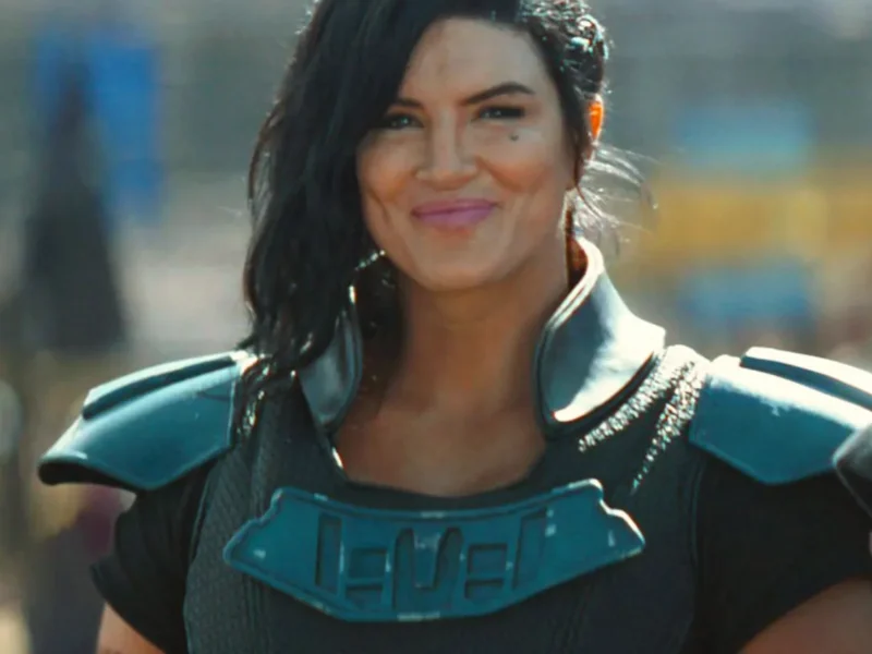 Personne vêtue d'une armure futuriste avec des épaulettes, cheveux noirs coiffés sur le côté, debout à l'extérieur et souriante, rappelant le personnage emblématique de Gina Carano chez Disney.