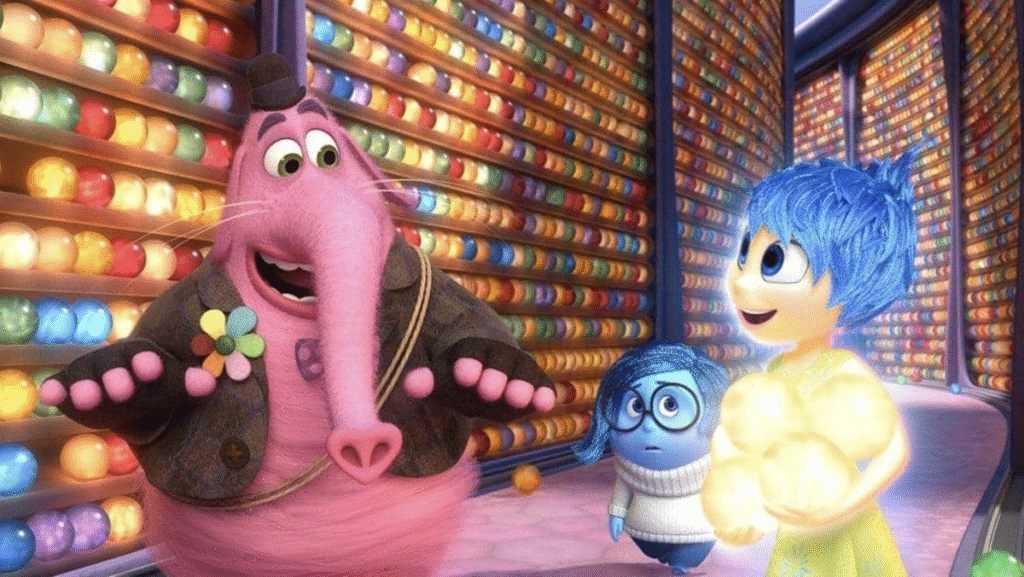 Trois personnages animés - Joie, Tristesse et Bing Bong - se tiennent dans une pièce colorée bordée d'orbes de mémoire lumineuses tirées d'Inside Out, également connu sous le nom de Vice-Versa.