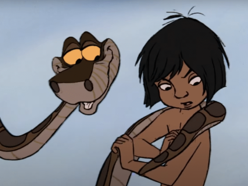 Un garçon animé aux cheveux noirs est enveloppé par un grand serpent qui le regarde en souriant et en murmurant "aie confiance". L'arrière-plan est un simple ciel bleu.