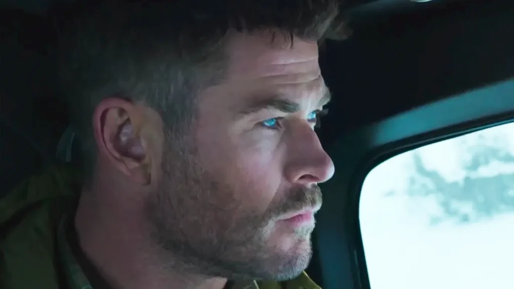 Un homme aux cheveux bruns courts et à la barbe regarde attentivement par la fenêtre alors qu'il est assis dans un véhicule, rappelant Chris Hemsworth dans Limitless de Disney+.
