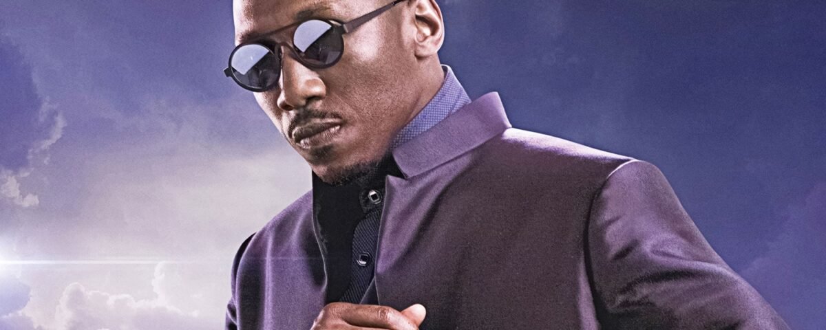 Un homme portant des lunettes de soleil et une veste sombre se tient sur un fond de ciel nuageux. Il incarne la présence confiante du Blade de Marvel, rappelant le style emblématique de Mahershala Ali.