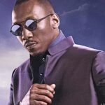 Un homme portant des lunettes de soleil et une veste sombre se tient sur un fond de ciel nuageux. Il incarne la présence confiante du Blade de Marvel, rappelant le style emblématique de Mahershala Ali.