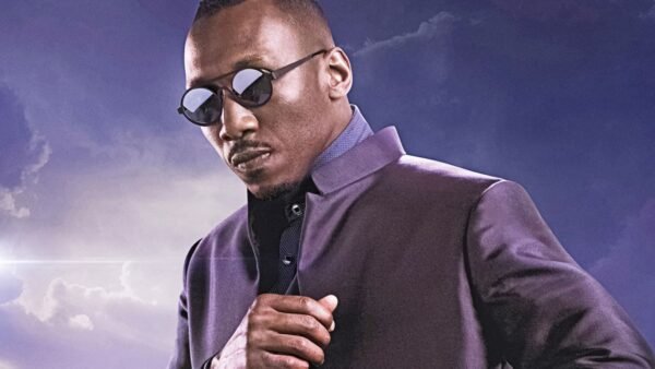 Un homme portant des lunettes de soleil et une veste sombre se tient sur un fond de ciel nuageux. Il incarne la présence confiante du Blade de Marvel, rappelant le style emblématique de Mahershala Ali.