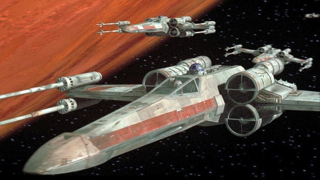 Trois chasseurs X-wing de la Guerre des étoiles s'élancent en formation dans l'espace et passent à côté d'une grande planète orange.