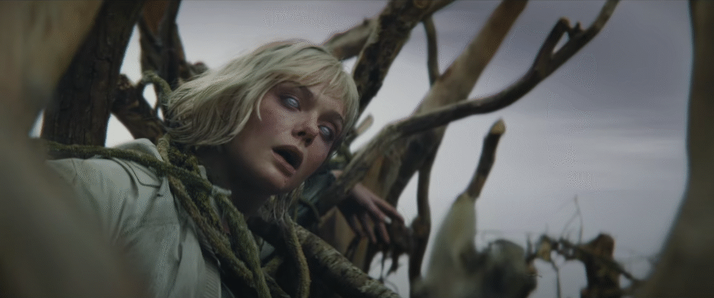 Une femme à la peau pâle et aux cheveux blonds apparaît sans vie, enchevêtrée dans des branches d'arbres et des lianes sous un ciel nuageux, rappelant une scène obsédante de Predator Badlands.