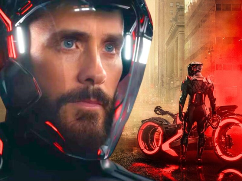 Un homme portant un casque futuriste est montré de près, avec une moto éclairée au néon et une personne portant un costume similaire dans une rue brumeuse et éclairée en rouge de la ville. Cette image évoque l'univers high-tech de Tron : Ares de Disney.