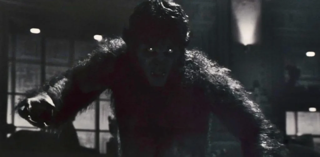 Un loup-garou aux yeux brillants et aux dents acérées se tient voûté dans une pièce faiblement éclairée, évoquant la présence inquiétante de Marvel's Werewolf By Night (Le loup-garou de nuit).