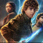 Trois jeunes gens se tiennent ensemble, chacun tenant une arme, tandis que des éclairs bleus et orange crépitent derrière eux dans cette scène saisissante de la bande-annonce de Percy Jackson Saison 2 sur Disney+.