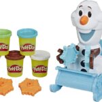 Six pots de Play-Doh, deux moules à flocons de neige orange et une figurine d'Olaf de la série Disney Frozen de Hasbro sont assis dans un traîneau bleu tenant un moule à flocons de neige.