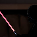 Une personne déguisée en Dark Vador tient un Sabre Laser Dark Vador sur un fond sombre, capturant le look emblématique de Star Wars.