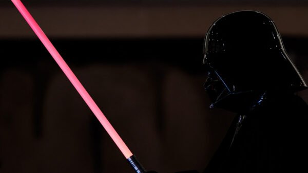 Une personne déguisée en Dark Vador tient un Sabre Laser Dark Vador sur un fond sombre, capturant le look emblématique de Star Wars.