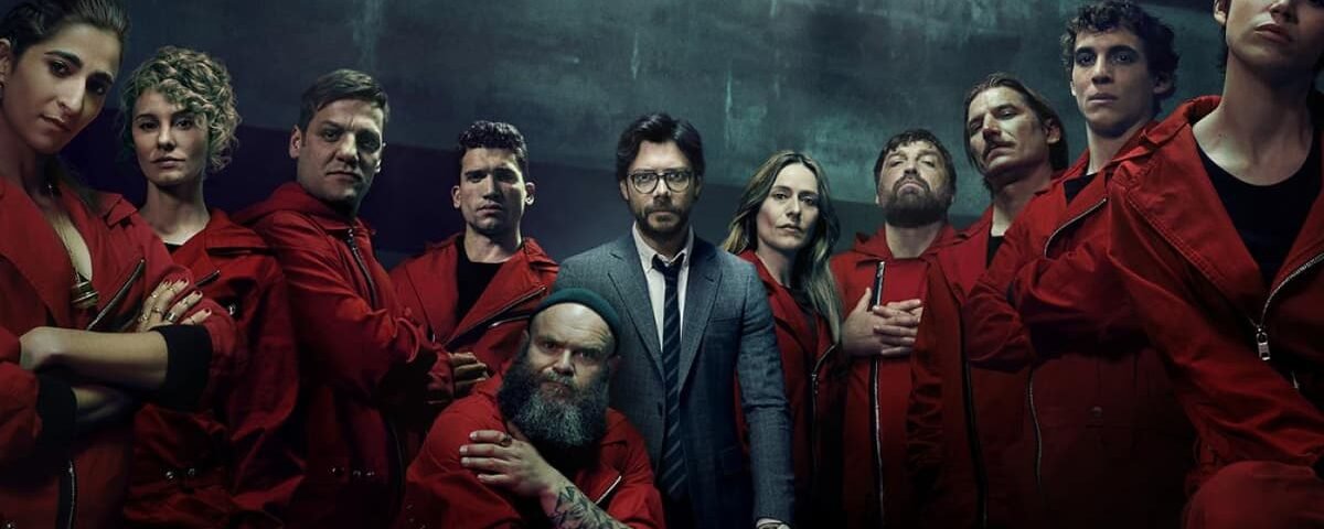 Un groupe de personnes portant des combinaisons rouges et un homme en costume se tiennent ensemble dans une pièce faiblement éclairée, regardant directement la caméra, ce qui rappelle les contenus espagnols populaires disponibles sur Disney+ Espagne.