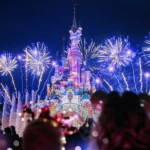 Des feux d'artifice illuminent le ciel nocturne au-dessus d'un château illuminé à Disneyland Paris, avec des silhouettes de spectateurs au premier plan pendant la parade magique de Noël Enchanté Disney.