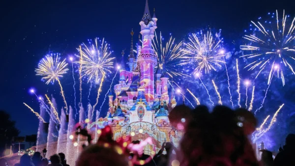 Des feux d'artifice illuminent le ciel nocturne au-dessus d'un château illuminé à Disneyland Paris, avec des silhouettes de spectateurs au premier plan pendant la parade magique de Noël Enchanté Disney.