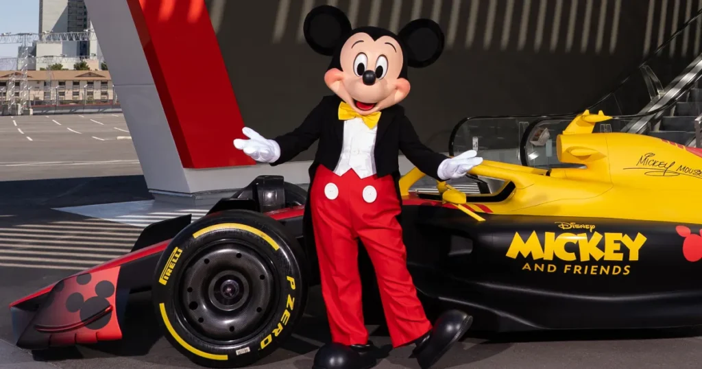 Une personne déguisée en Mickey Mouse se tient à côté d'une voiture de course de F1 jaune et noire portant l'inscription "Mickey and Friends", illustrant le partenariat dynamique entre Disney et le sport automobile.