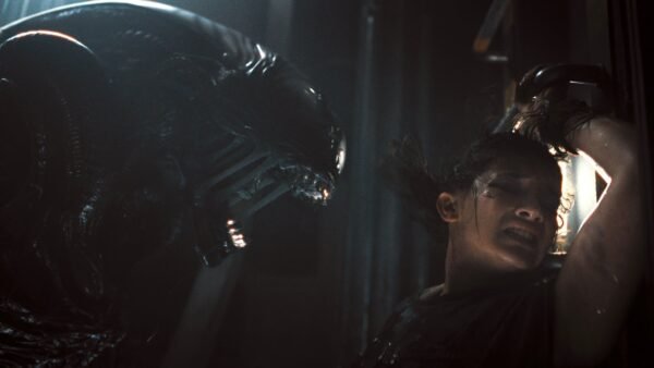 Une femme se presse contre un mur, effrayée, tandis qu'une grande créature extraterrestre menaçante - rappelant Alien Romulus - s'agite près d'elle dans un espace faiblement éclairé. Ce film illustre bien le style de suspense que le réalisateur Fede Álvarez apporte à la franchise Disney.