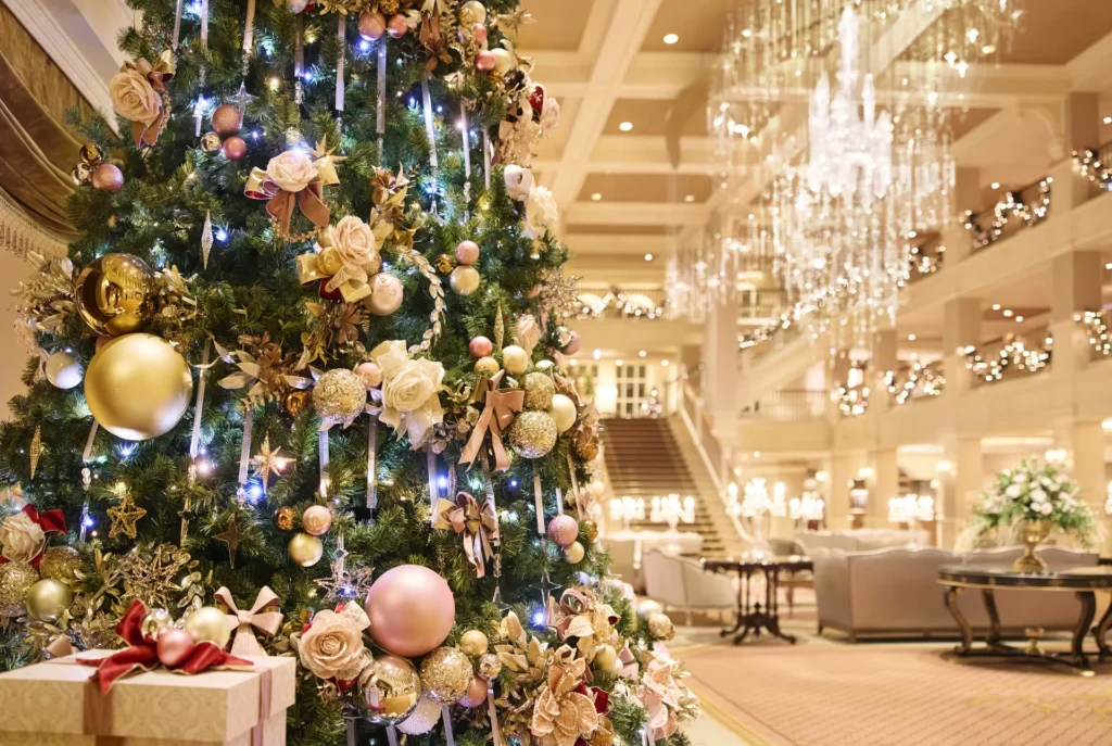 Un sapin de Noël décoré d'ornements et de rubans dorés se dresse dans le hall d'un hôtel élégant et festif de Disneyland Paris, rayonnant de la magie de Noël Enchanté, avec des cadeaux emballés en dessous.
