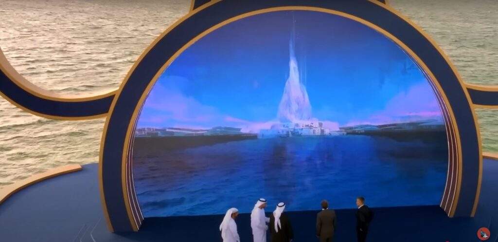 Quatre hommes, trois en robe blanche et un en costume noir, se tiennent sur une scène au bord de la mer et regardent un écran numérique affichant le concept ultramoderne du Château Disney Abu Dhabi, dont l'ouverture est prévue pour 2030.